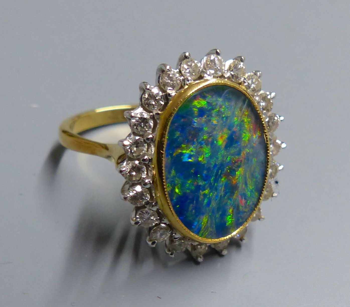 An 18ct, black opal doublet and diamond set oval cluster ring, size M, gross 7.3 grams.